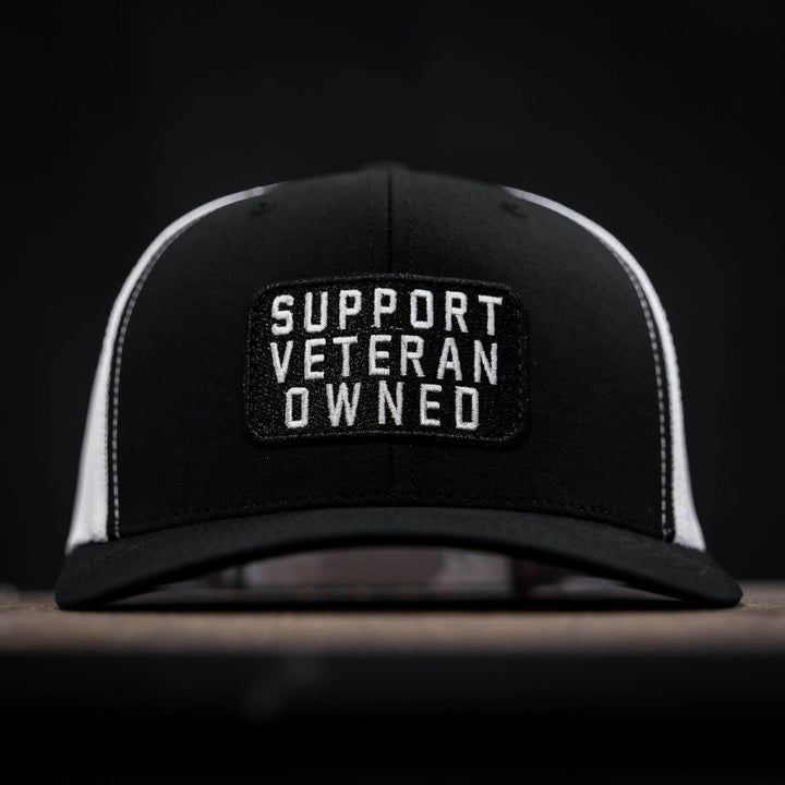 A mid-profile mesh snapback with a patch that says “Support veteran owned” in white letters #color_black-white