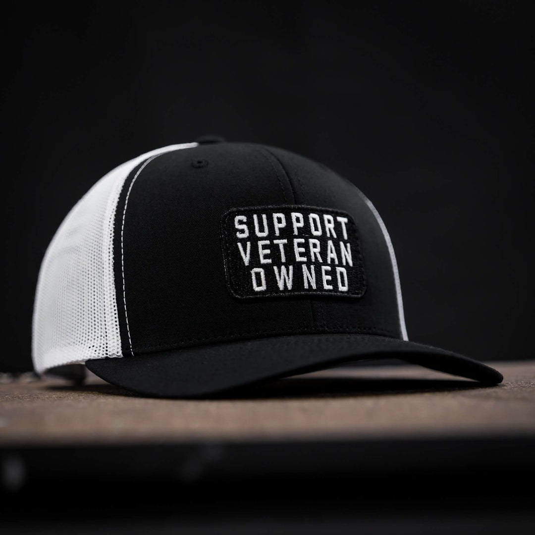 A mid-profile mesh snapback with a patch that says “Support veteran owned” in white letters #color_black-white