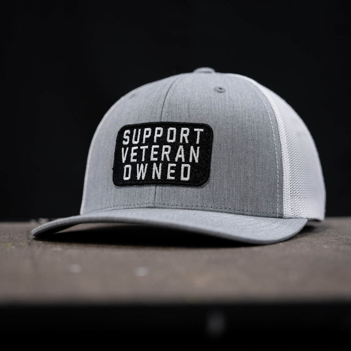 A mid-profile mesh snapback with a patch that says “Support veteran owned” in white letters #color_gray-white
