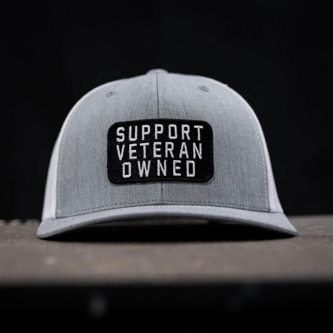 A black mid-profile mesh snapback with a patch that says “Support veteran owned” in white letters #color_gray-white