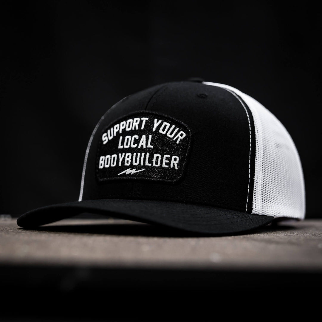 A black and white mid-profile mesh snapback with a patch that reads “Support your local bodybuilder”