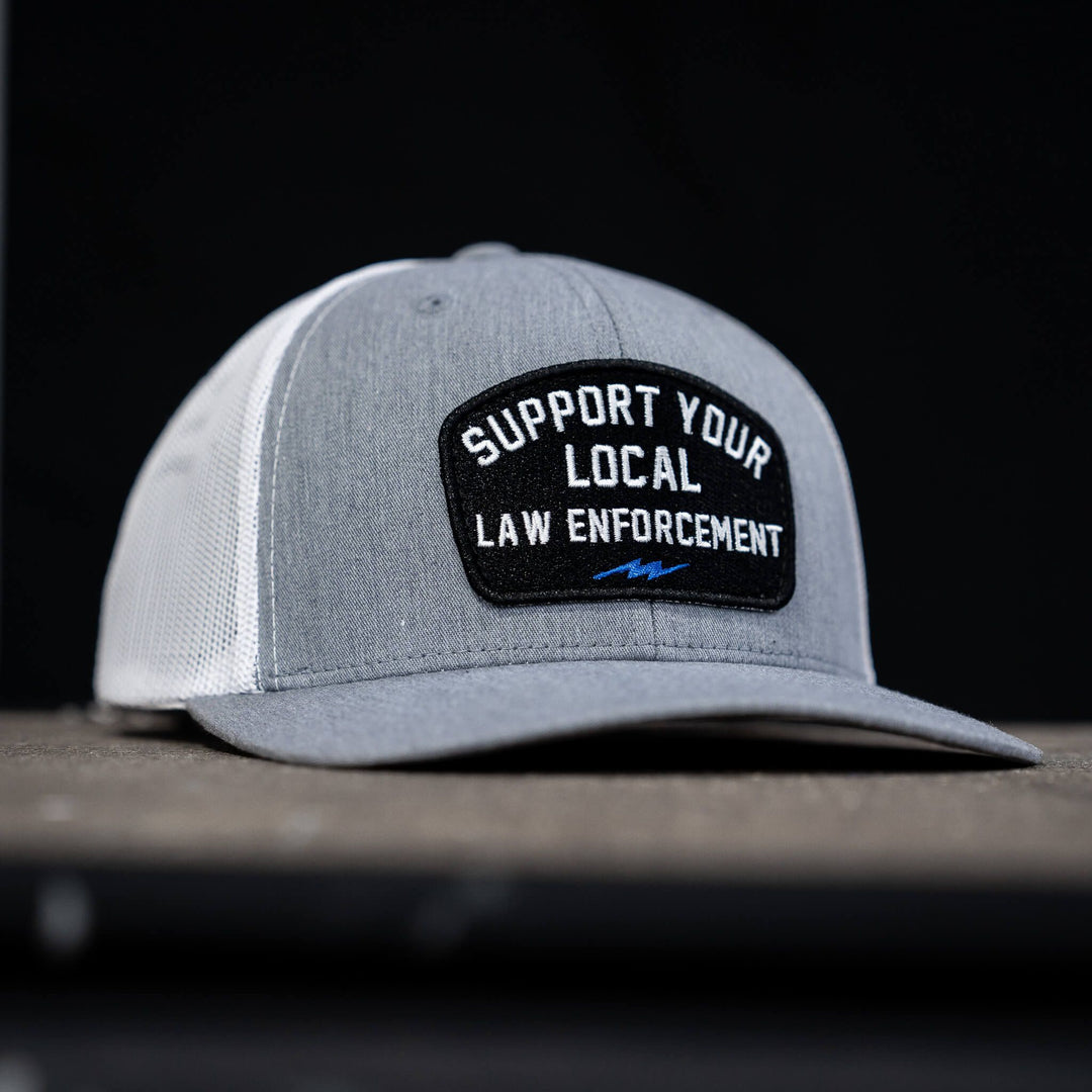 A mid-profile snapback hat with a patch on the front that says “Support your local law enforcement” #color_gray-white