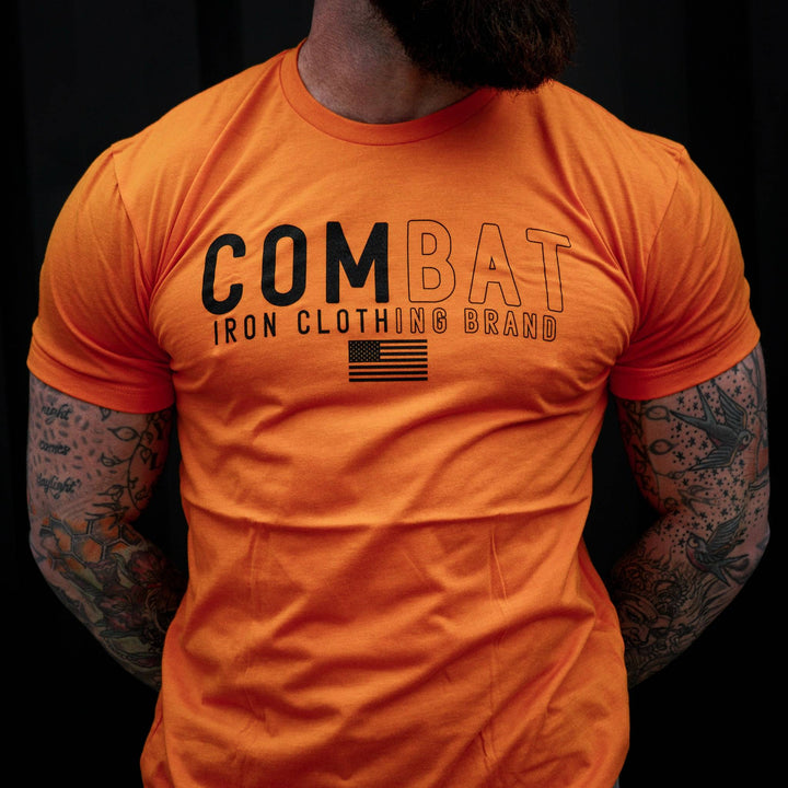 Men’s orange t-shirt with the words “Combat Iron clothing brand” on the front and an American flag #color_orange